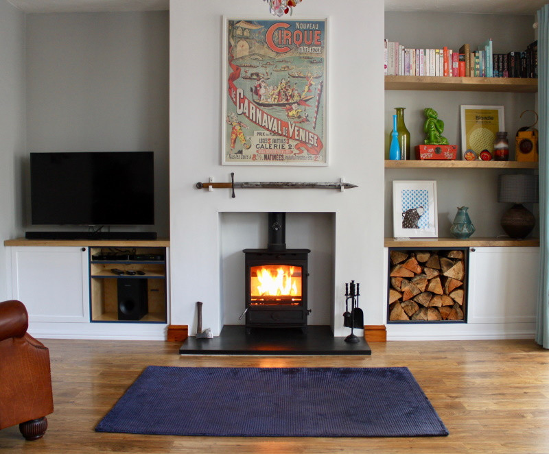 Photo of a mid-sized country enclosed living room in West Midlands with grey walls, laminate floors, a wood stove, a plaster fireplace surround, a built-in media wall and brown floor.