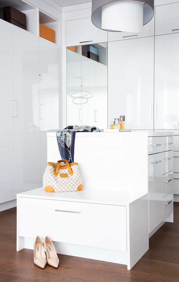 Exemple d'un dressing room tendance pour une femme avec un placard à porte plane, des portes de placard blanches, parquet foncé et un sol marron.