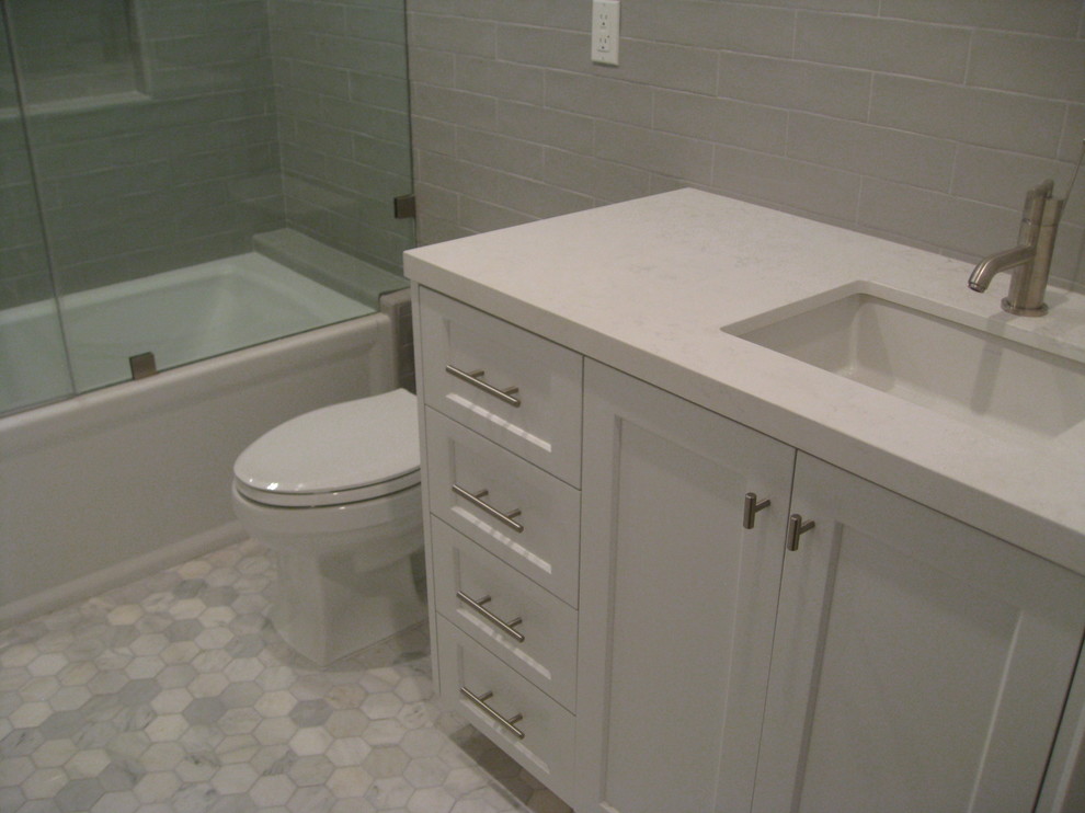 This is an example of a mid-sized transitional 3/4 bathroom in Los Angeles with shaker cabinets, white cabinets, an alcove tub, an alcove shower, a two-piece toilet, grey walls, marble floors, an undermount sink, white floor, a hinged shower door and white benchtops.