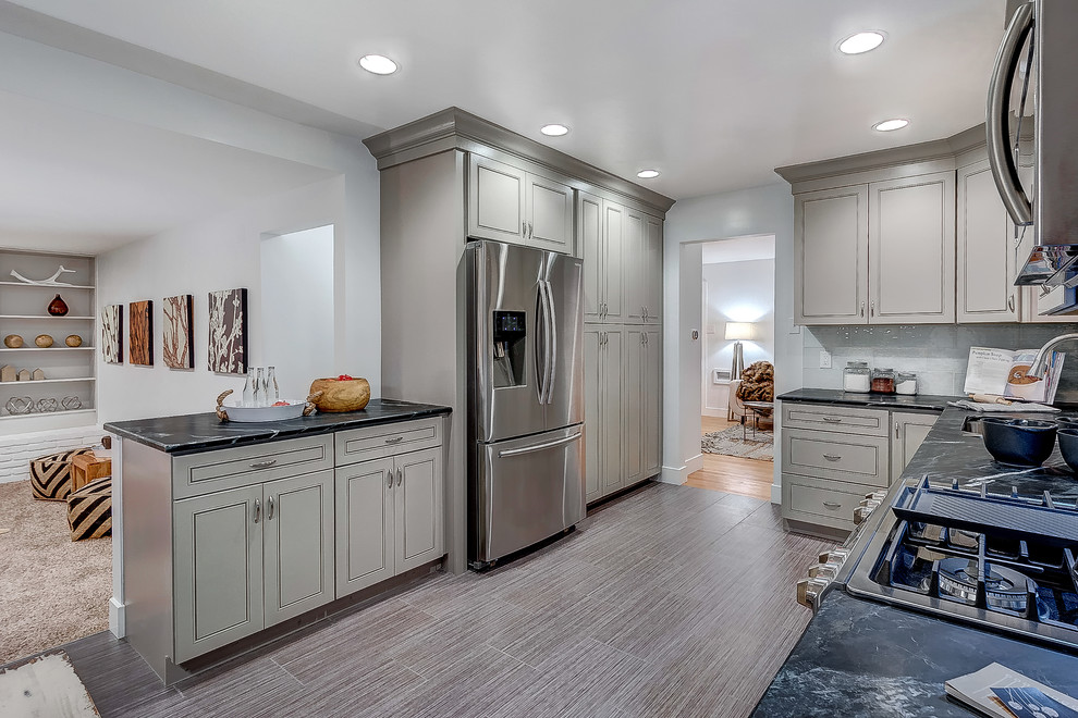 Inspiration for a large transitional u-shaped porcelain tile kitchen remodel in Denver with an undermount sink, raised-panel cabinets, gray cabinets, soapstone countertops, gray backsplash, glass tile backsplash, stainless steel appliances and no island
