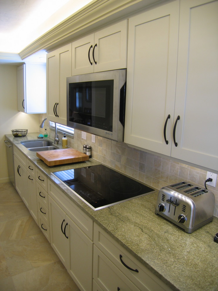 Photo of a small transitional galley kitchen in Tampa with an undermount sink, shaker cabinets, white cabinets, granite benchtops, beige splashback, porcelain splashback, stainless steel appliances and porcelain floors.