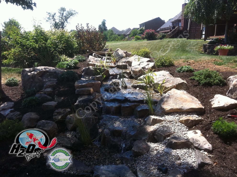 This is an example of a large eclectic backyard shaded garden in Louisville with a water feature and mulch.