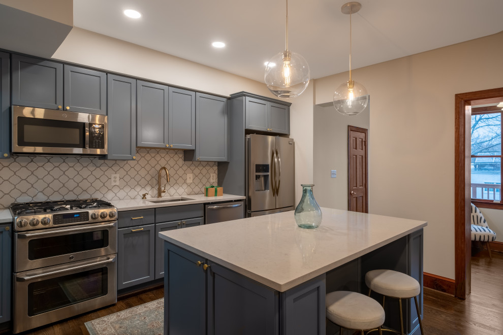 Small modern single-wall kitchen pantry in DC Metro with a single-bowl sink, shaker cabinets, grey cabinets, quartz benchtops, white splashback, ceramic splashback, stainless steel appliances, dark hardwood floors, with island, brown floor and white benchtop.
