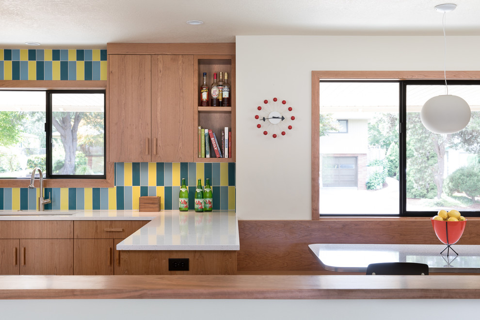 Large midcentury u-shaped eat-in kitchen in Portland with an undermount sink, flat-panel cabinets, medium wood cabinets, multi-coloured splashback, ceramic splashback, stainless steel appliances, light hardwood floors, a peninsula, white benchtop and recycled glass benchtops.
