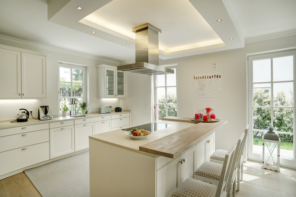 Large traditional kitchen in Munich with a drop-in sink, recessed-panel cabinets, white cabinets, panelled appliances, medium hardwood floors and with island.