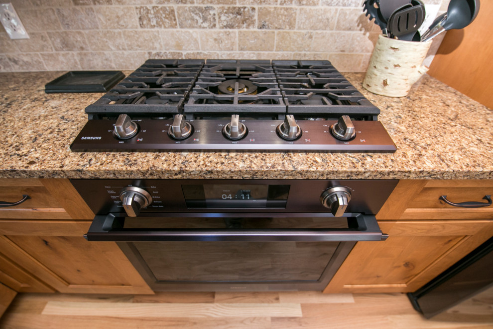 Mid-sized mountain style galley medium tone wood floor and brown floor eat-in kitchen photo in Denver with an undermount sink, shaker cabinets, medium tone wood cabinets, quartz countertops, gray backsplash, stone tile backsplash, black appliances, no island and brown countertops