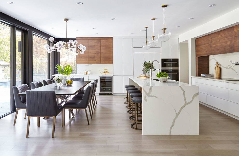 Design ideas for a contemporary l-shaped open plan kitchen in Toronto with flat-panel cabinets, white cabinets, quartzite benchtops, white splashback, stone slab splashback, stainless steel appliances, light hardwood floors, with island, brown floor and an undermount sink.