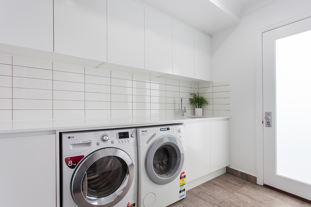 Design ideas for a contemporary galley dedicated laundry room in Other with a farmhouse sink, flat-panel cabinets, white cabinets, white walls, ceramic floors, a side-by-side washer and dryer and brown floor.