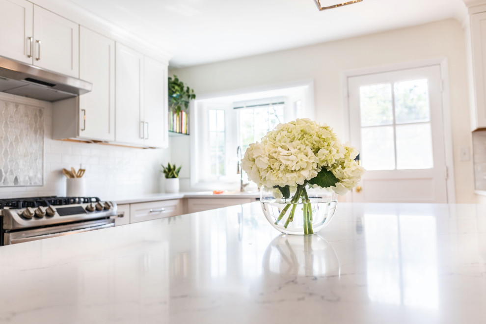 Mid-sized transitional l-shaped light wood floor and brown floor eat-in kitchen photo in Baltimore with an undermount sink, shaker cabinets, white cabinets, quartz countertops, white backsplash, marble backsplash, stainless steel appliances, an island and white countertops