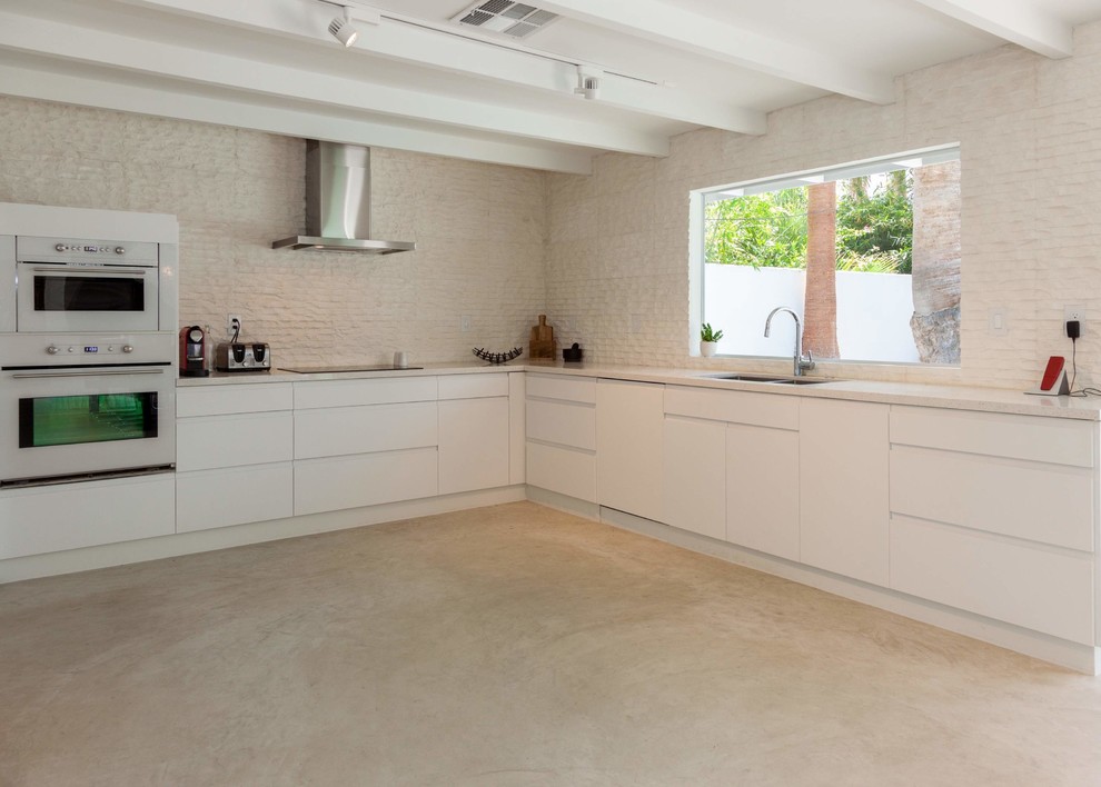 Design ideas for a contemporary l-shaped open plan kitchen in Los Angeles with a double-bowl sink, flat-panel cabinets, white cabinets, quartz benchtops, white splashback, stone tile splashback, white appliances, concrete floors and no island.