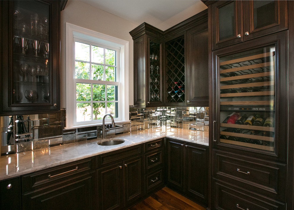 Photo of a large traditional kitchen in New Orleans with a double-bowl sink, raised-panel cabinets, dark wood cabinets, quartzite benchtops, metallic splashback, mirror splashback, panelled appliances and dark hardwood floors.