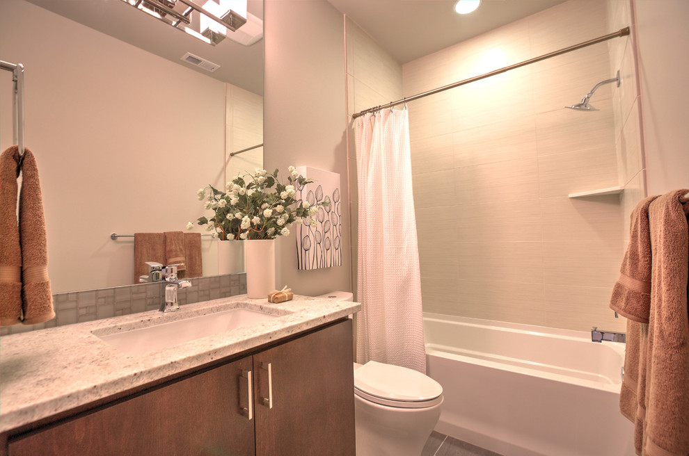 Design ideas for a mid-sized contemporary bathroom in Seattle with an undermount sink, flat-panel cabinets, medium wood cabinets, granite benchtops, a shower/bathtub combo, a one-piece toilet, gray tile, glass tile and grey walls.