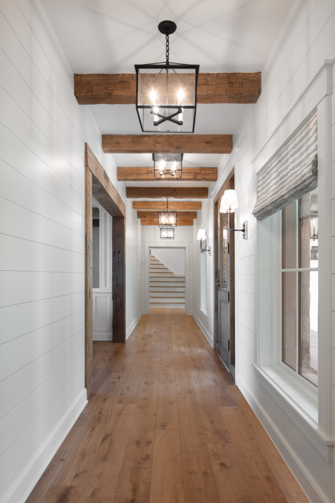 Immagine di un ampio ingresso o corridoio country con pareti bianche, pavimento in legno massello medio, pavimento marrone, travi a vista e pannellatura