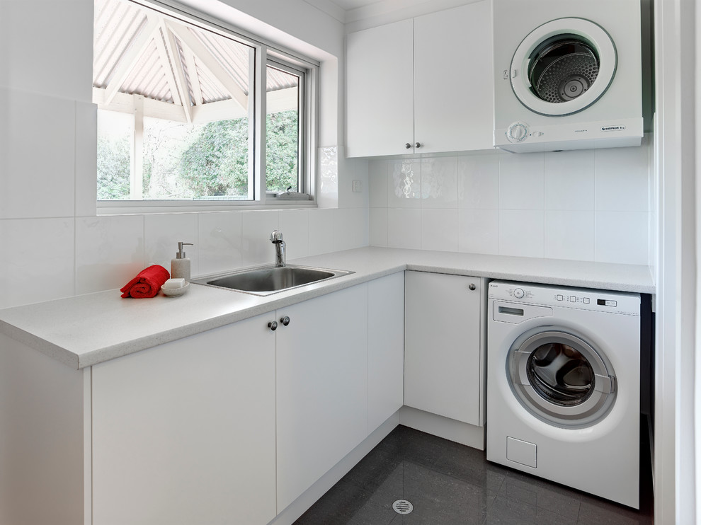 Mid-sized contemporary l-shaped dedicated laundry room in Other with a single-bowl sink, white cabinets, laminate benchtops, white walls, porcelain floors and a stacked washer and dryer.