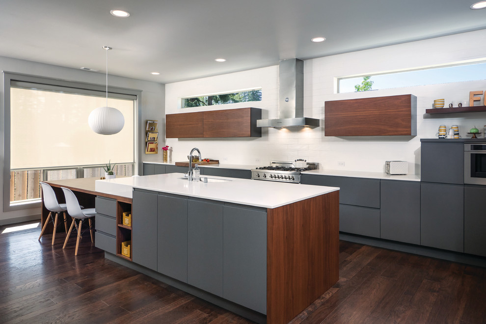 This is an example of a contemporary galley kitchen in Seattle with an undermount sink, flat-panel cabinets, grey cabinets, white splashback, subway tile splashback, stainless steel appliances, dark hardwood floors, with island and quartz benchtops.