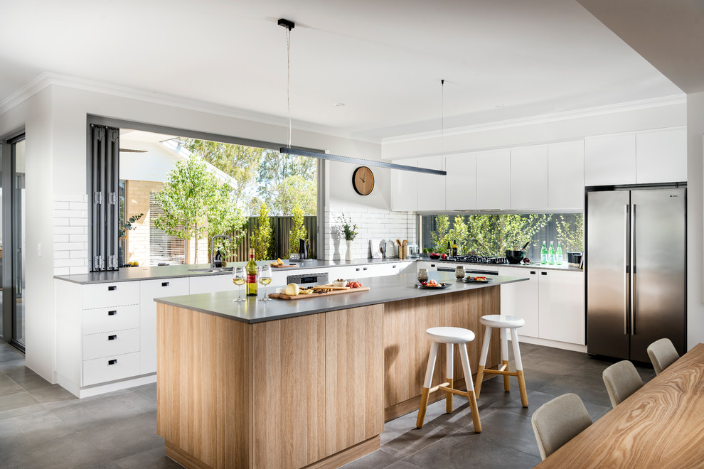 Inspiration for a contemporary l-shaped open plan kitchen in Perth with flat-panel cabinets, white cabinets, white splashback, subway tile splashback, stainless steel appliances, concrete floors, with island and grey floor.