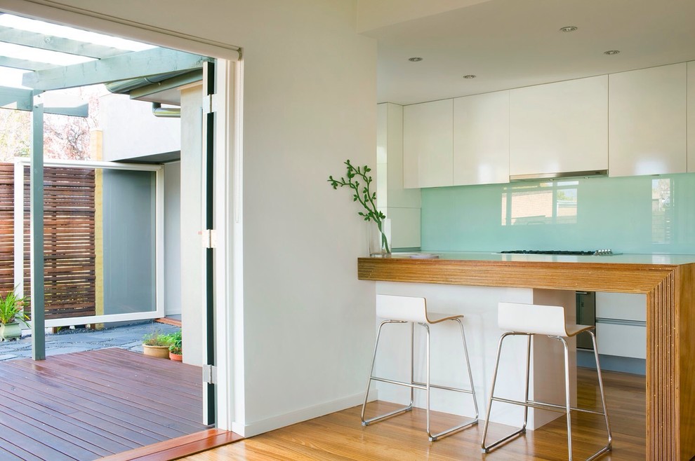 Photo of a contemporary kitchen in Melbourne with flat-panel cabinets, white cabinets, wood benchtops and glass sheet splashback.