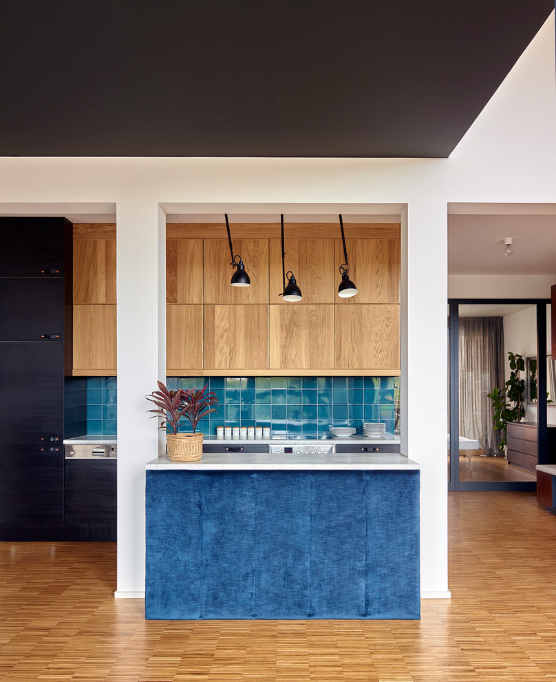 This is an example of a small contemporary open plan kitchen in Berlin with flat-panel cabinets, blue splashback, ceramic splashback, medium hardwood floors, with island and blue cabinets.