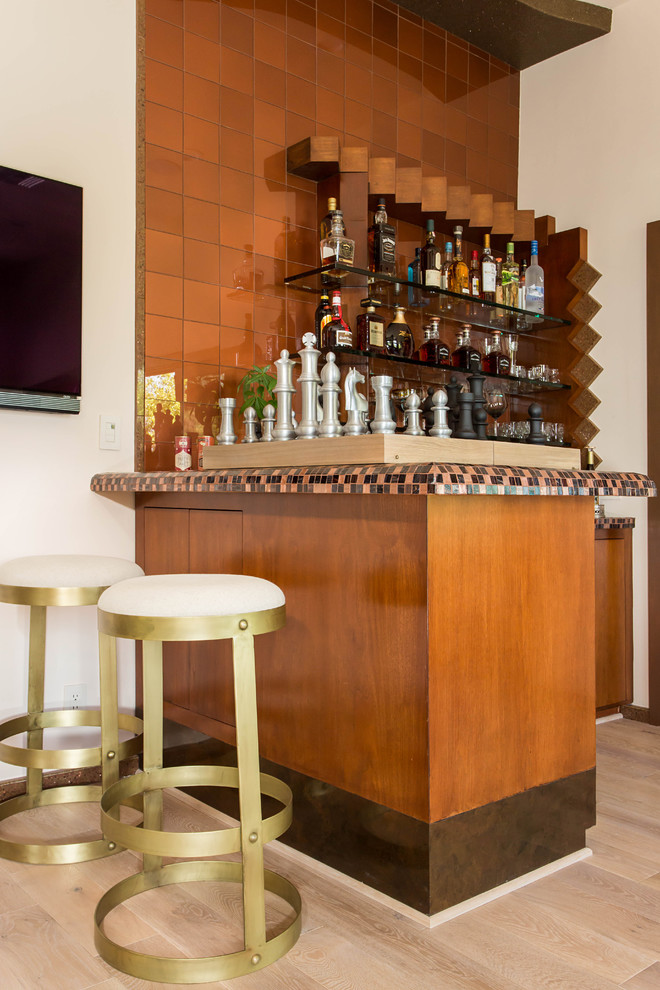 Photo of a mid-sized eclectic l-shaped home bar in Los Angeles with a drop-in sink, flat-panel cabinets, medium wood cabinets, tile benchtops, glass tile splashback and light hardwood floors.