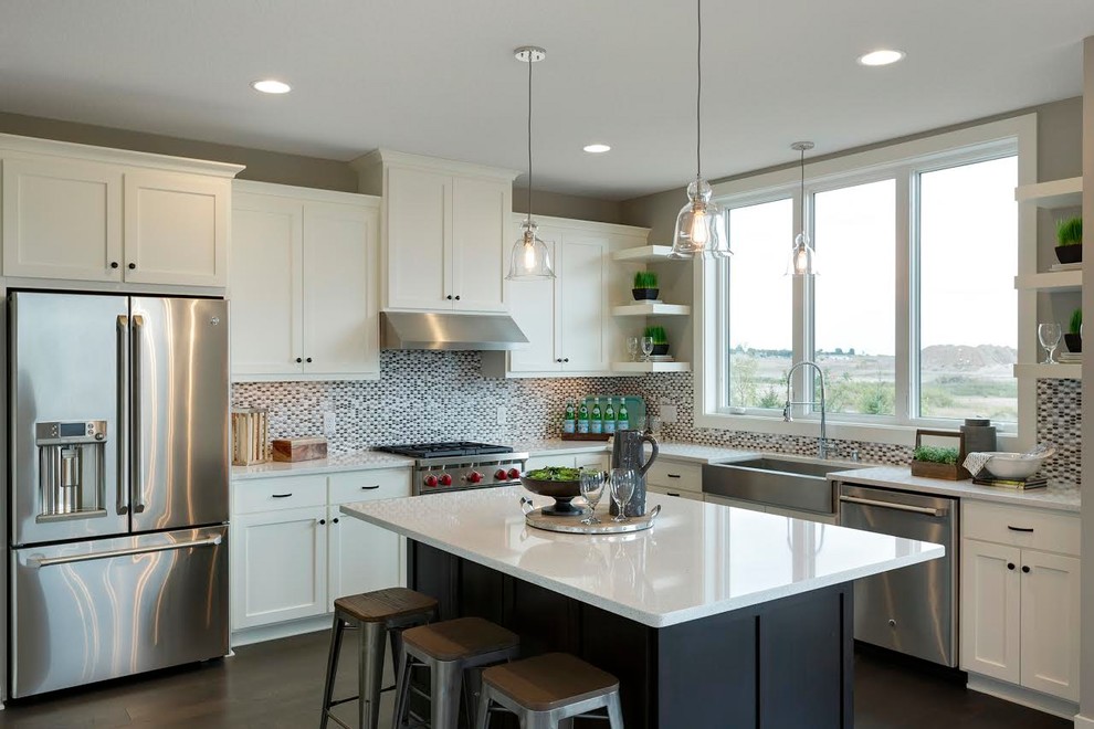 Example of a mid-sized transitional l-shaped dark wood floor and brown floor kitchen design in Minneapolis with a farmhouse sink, shaker cabinets, white cabinets, quartz countertops, multicolored backsplash, mosaic tile backsplash, stainless steel appliances and an island