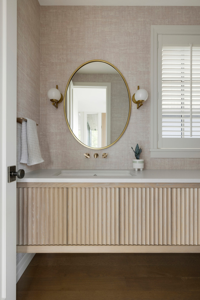 Example of a mid-sized transitional light wood floor, single-sink and wallpaper bathroom design in Minneapolis with furniture-like cabinets, light wood cabinets, a two-piece toilet, pink walls, an undermount sink, concrete countertops, beige countertops and a built-in vanity