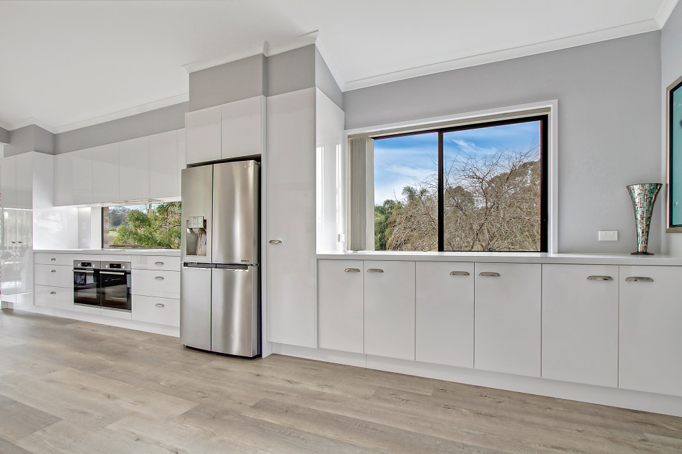 Foto på ett stort funkis vit linjärt kök och matrum, med en undermonterad diskho, släta luckor, vita skåp, bänkskiva i kvarts, rostfria vitvaror och en köksö