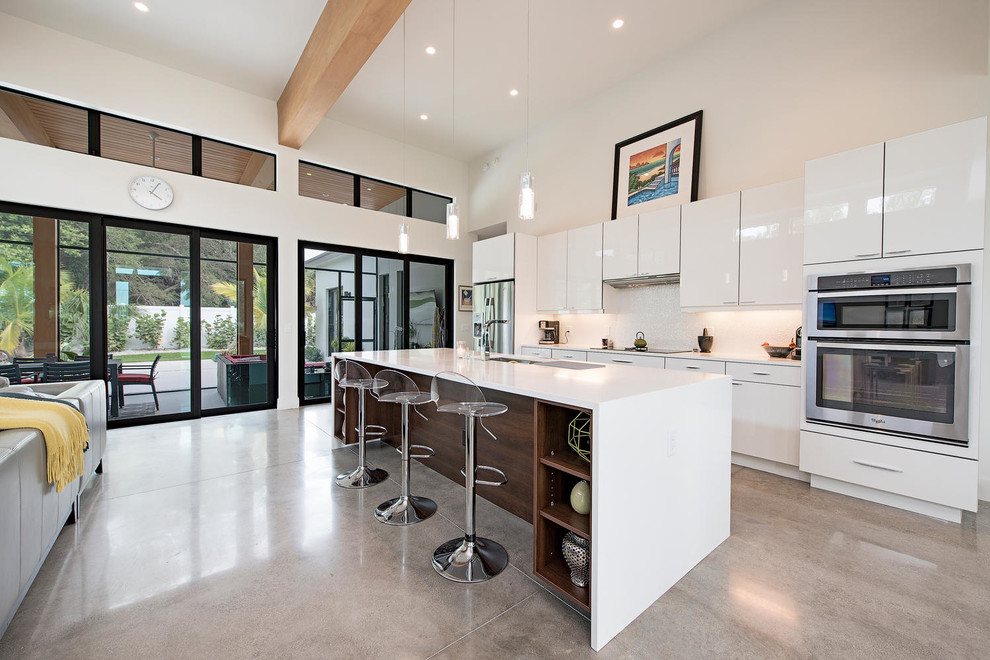 Photo of a mid-sized modern galley eat-in kitchen in Miami with an integrated sink, flat-panel cabinets, white cabinets, quartzite benchtops, white splashback, stainless steel appliances, concrete floors and with island.