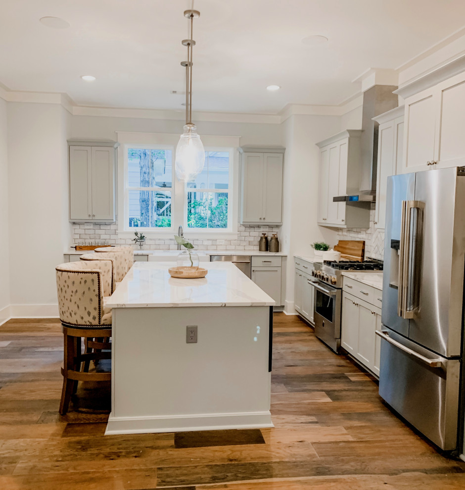 Inspiration for a mid-sized transitional l-shaped brown floor eat-in kitchen remodel with a farmhouse sink, shaker cabinets, gray cabinets, quartz countertops, gray backsplash, ceramic backsplash, stainless steel appliances, an island and white countertops