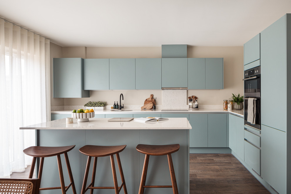Photo of a contemporary l-shaped kitchen in Buckinghamshire with a submerged sink, flat-panel cabinets, blue cabinets, stainless steel appliances, dark hardwood flooring, an island, brown floors and white worktops.