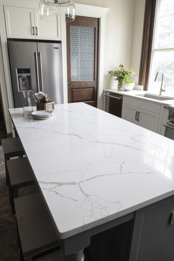 Example of a transitional l-shaped kitchen design with an undermount sink, quartz countertops, white backsplash, stone slab backsplash, stainless steel appliances, an island and white countertops