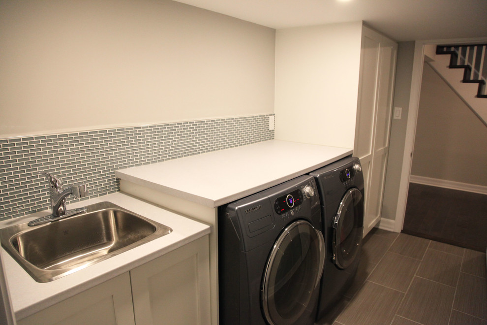 Photo of a mid-sized modern single-wall dedicated laundry room in Ottawa with grey walls, a drop-in sink, recessed-panel cabinets, white cabinets, solid surface benchtops, ceramic floors and a side-by-side washer and dryer.