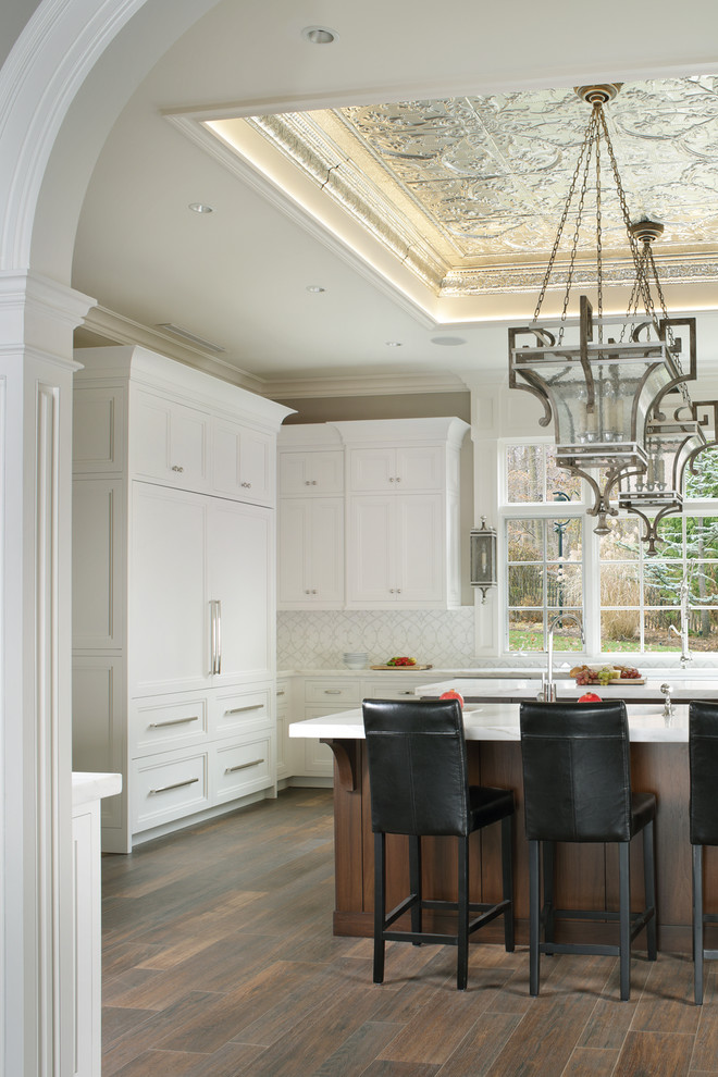 Design ideas for a large transitional kitchen in New York with a farmhouse sink, recessed-panel cabinets, white cabinets, marble benchtops, white splashback, stone tile splashback, stainless steel appliances, porcelain floors and multiple islands.