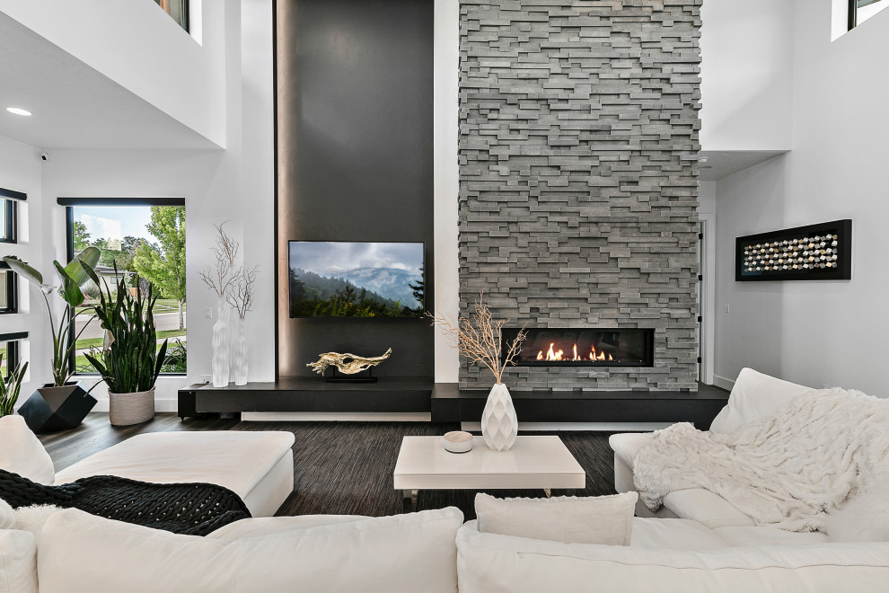 Inspiration for an expansive modern formal open plan living room in Boise with a standard fireplace, a stacked stone fireplace surround, a vaulted ceiling, white walls, medium hardwood flooring, beige floors, a wall mounted tv and panelled walls.
