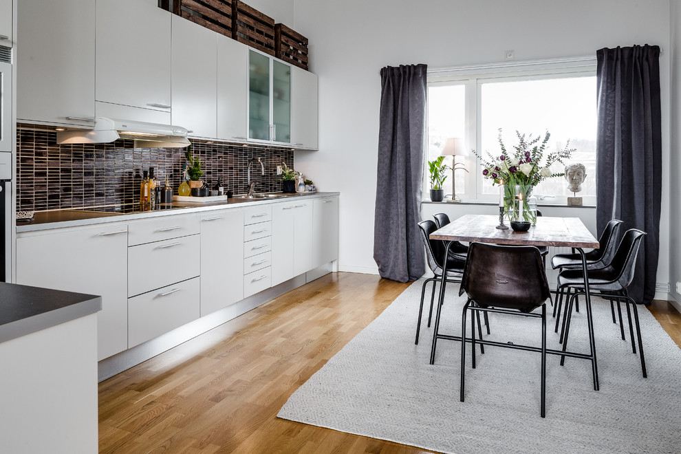 Inspiration for a large scandinavian l-shaped eat-in kitchen in Gothenburg with a drop-in sink, flat-panel cabinets, white cabinets, brown splashback, stainless steel appliances, light hardwood floors and no island.