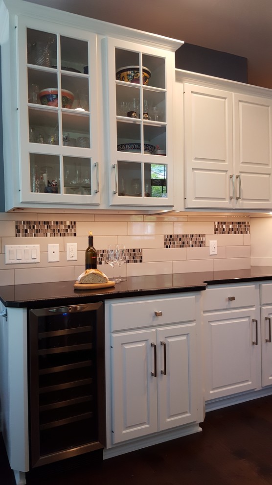 Inspiration for a mid-sized transitional l-shaped medium tone wood floor and brown floor kitchen remodel with an undermount sink, raised-panel cabinets, white cabinets, granite countertops, white backsplash, subway tile backsplash, stainless steel appliances and an island