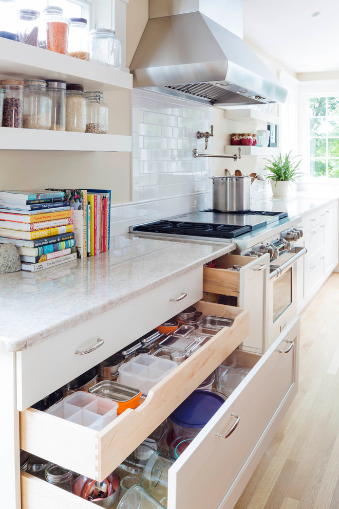 Kitchen - large transitional l-shaped light wood floor kitchen idea in Boston with a farmhouse sink, recessed-panel cabinets, white cabinets, quartz countertops, white backsplash, subway tile backsplash, stainless steel appliances and an island