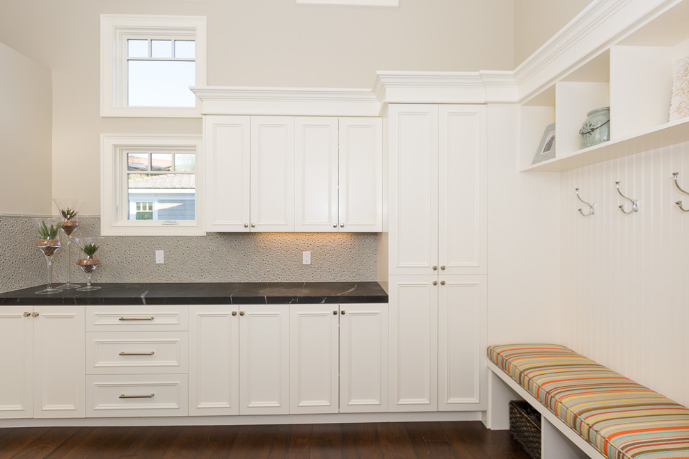 Photo of an expansive transitional l-shaped dedicated laundry room in Orange County with recessed-panel cabinets, white cabinets, soapstone benchtops, beige walls, medium hardwood floors and a side-by-side washer and dryer.