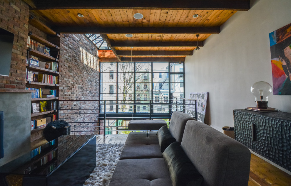Photo of a mid-sized industrial loft-style living room in Other with white walls, medium hardwood floors, a standard fireplace, a concrete fireplace surround, brown floor, exposed beam and brick walls.