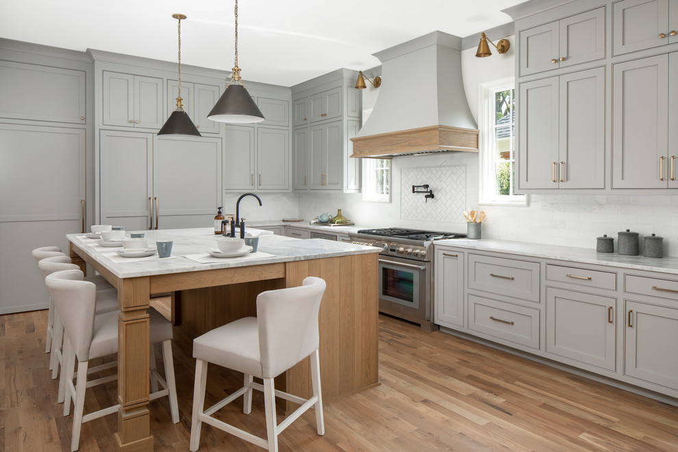 Design ideas for a large transitional l-shaped kitchen in Charlotte with beaded inset cabinets, grey cabinets, marble benchtops, stainless steel appliances, with island, white splashback, subway tile splashback, light hardwood floors and white benchtop.