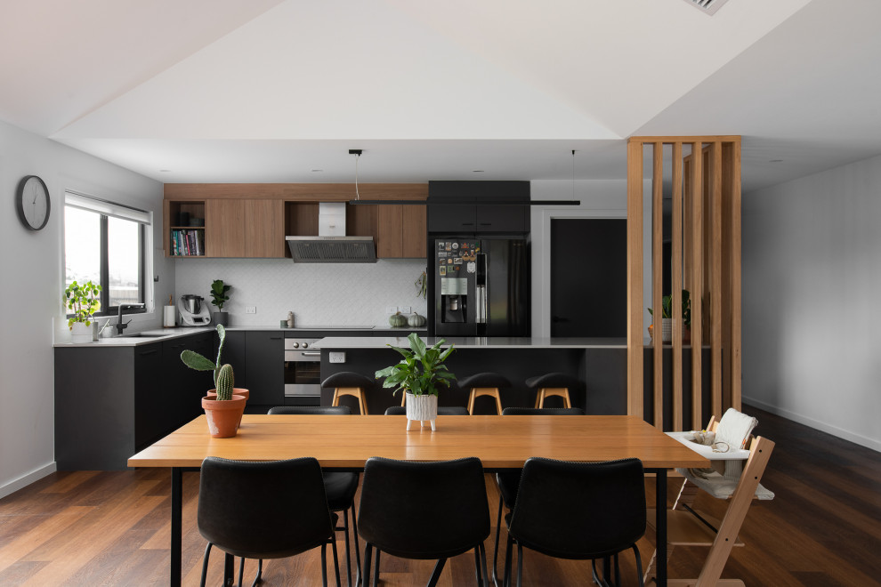 Contemporary l-shaped open plan kitchen in Hobart with an undermount sink, flat-panel cabinets, black cabinets, white splashback, stainless steel appliances, dark hardwood floors, with island, brown floor, grey benchtop and vaulted.