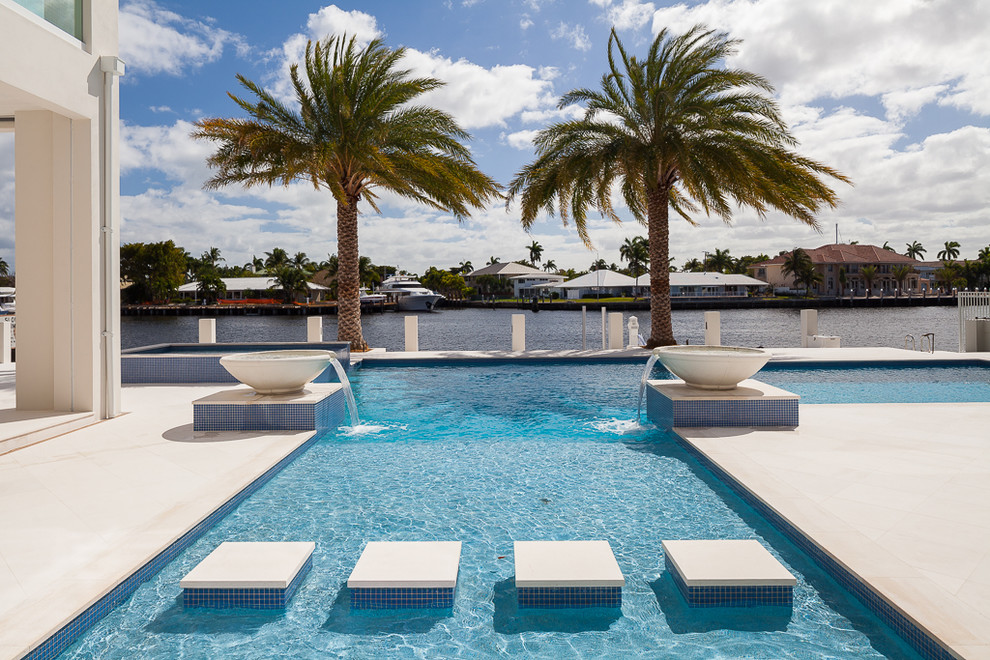 Inspiration for a contemporary backyard custom-shaped pool in Miami with natural stone pavers and a water feature.