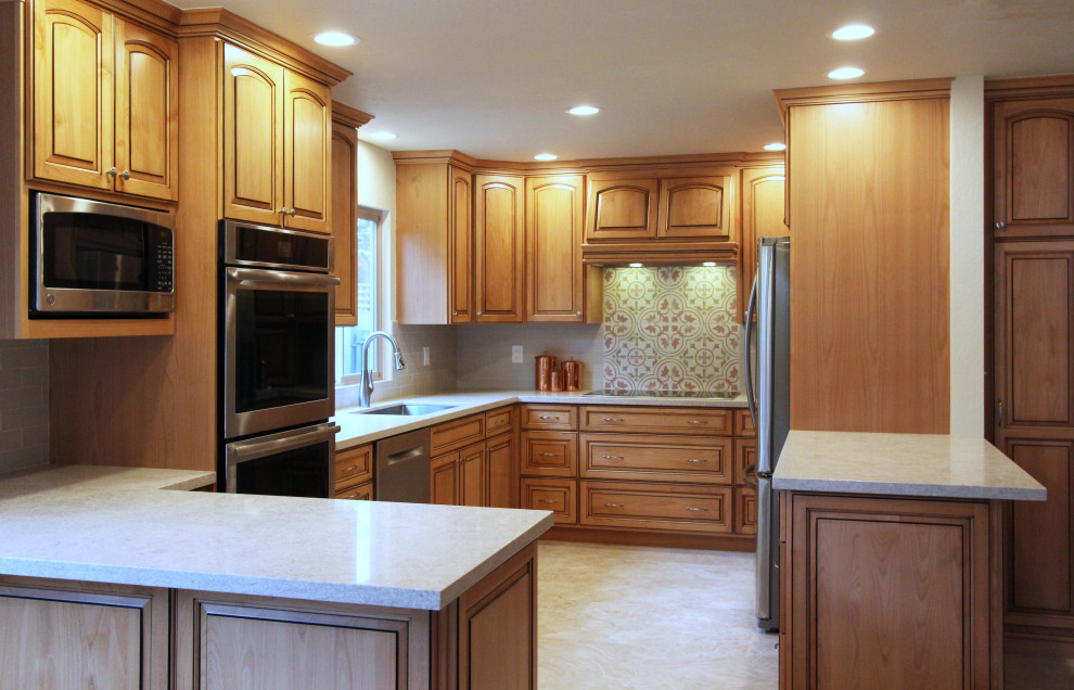 Mid-sized u-shaped porcelain tile and beige floor eat-in kitchen photo with an undermount sink, raised-panel cabinets, medium tone wood cabinets, quartz countertops, multicolored backsplash, ceramic backsplash, stainless steel appliances, a peninsula and multicolored countertops