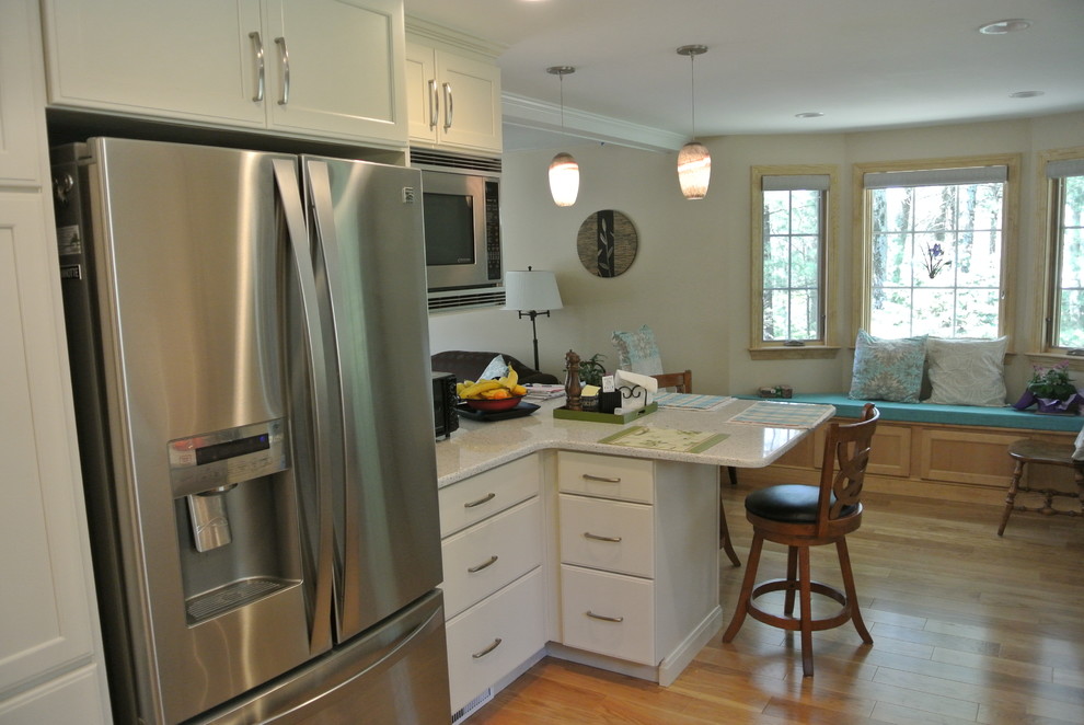 Example of a transitional l-shaped medium tone wood floor eat-in kitchen design in Boston with an undermount sink, shaker cabinets, white cabinets, recycled glass countertops, white backsplash, subway tile backsplash, stainless steel appliances, a peninsula and white countertops