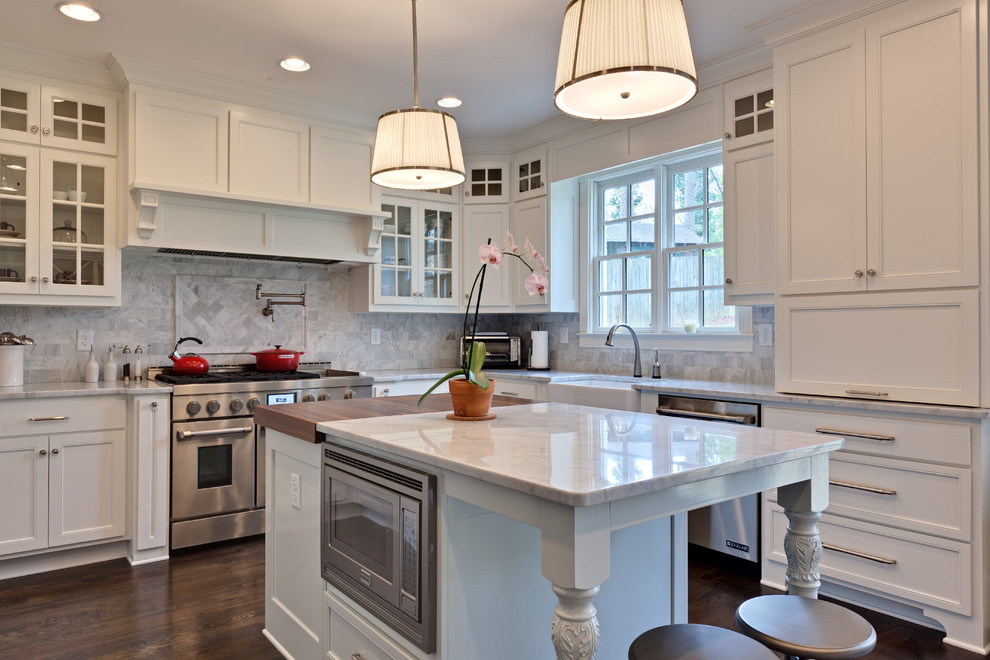 Photo of a mid-sized traditional u-shaped eat-in kitchen in Atlanta with a farmhouse sink, white cabinets, marble benchtops, white splashback, stone tile splashback, stainless steel appliances, dark hardwood floors, with island and recessed-panel cabinets.