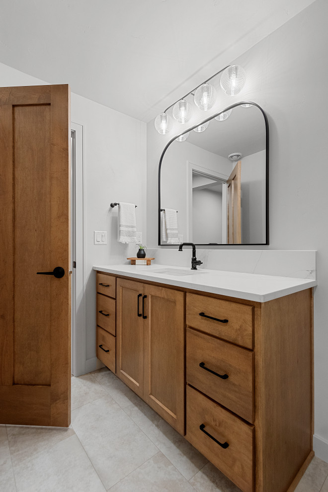 Mid-sized transitional kids' white tile vinyl floor, multicolored floor and single-sink bathroom photo with shaker cabinets, brown cabinets, a two-piece toilet, white walls, an undermount sink, quartz countertops, white countertops and a built-in vanity
