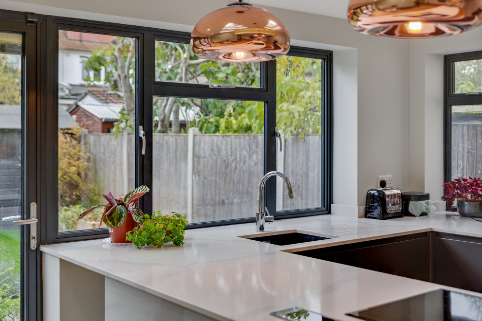 Photo of a mid-sized contemporary u-shaped eat-in kitchen in London with an undermount sink, flat-panel cabinets, grey cabinets, quartz benchtops, white splashback, engineered quartz splashback, stainless steel appliances, medium hardwood floors, a peninsula, white benchtop and vaulted.