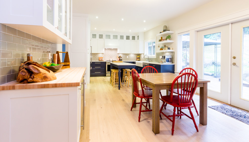 Open concept kitchen - large transitional u-shaped light wood floor open concept kitchen idea with a farmhouse sink, shaker cabinets, blue cabinets, quartz countertops, gray backsplash, glass tile backsplash, stainless steel appliances, an island and white countertops