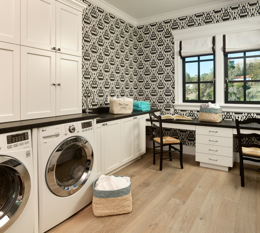 Transitional l-shaped laundry room in San Francisco with an undermount sink, shaker cabinets, white cabinets, multi-coloured walls, light hardwood floors, a side-by-side washer and dryer, beige floor and black benchtop.