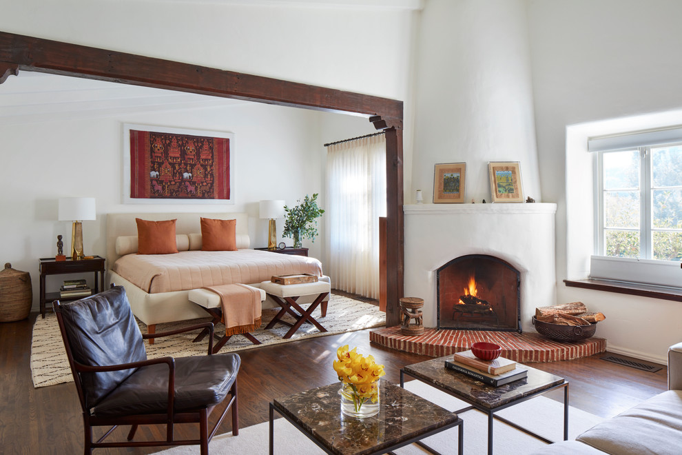 Inspiration for a mediterranean master bedroom in Los Angeles with white walls, a corner fireplace, a plaster fireplace surround, brown floor and dark hardwood floors.