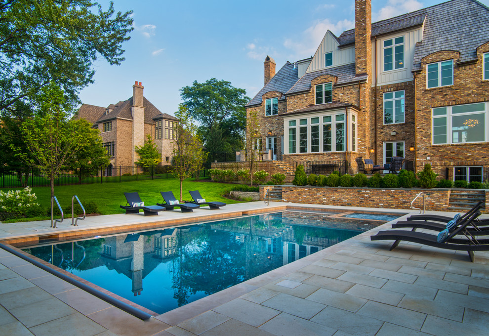 This is an example of a mid-sized traditional backyard rectangular pool in Chicago with a hot tub and natural stone pavers.